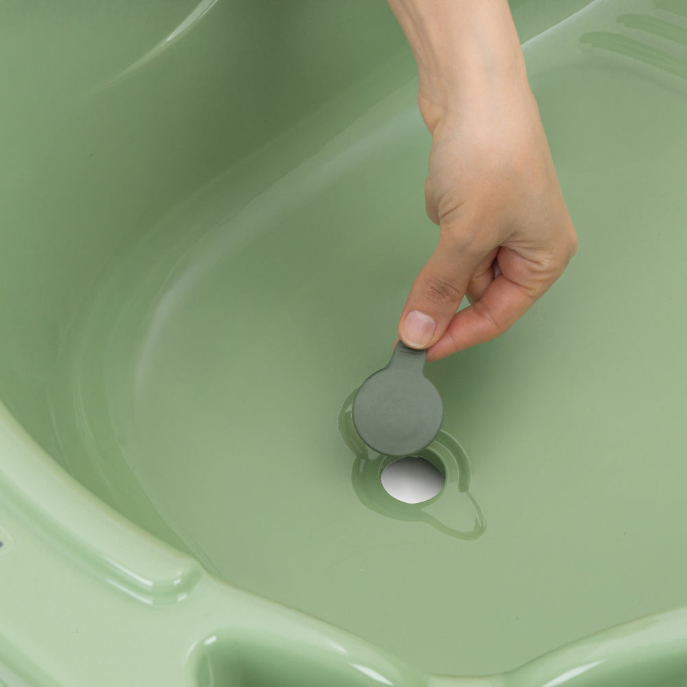 Hand holding a green bath bomb in a green bathtub